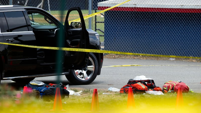 Bags lay on the ground near an automobile with a bullet hole in its windshield in the parking...